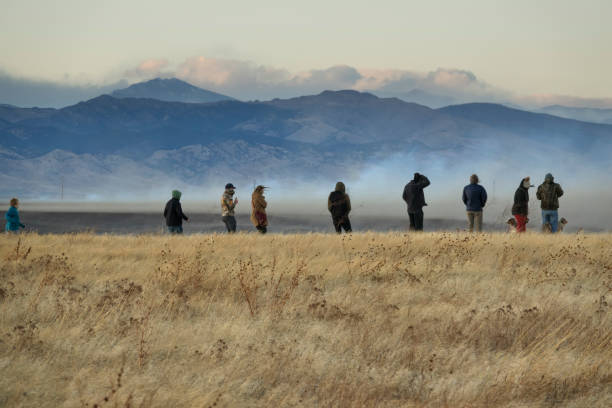 Lining up on the hillside, windblown watchers stand in front of the smoke cloud.
