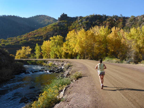 Running along the South Platte River on a dirt road, a woman with a ponytail and shorts enjoys the fall colors and cool temperatures in the Colorado Rocky Mountains.